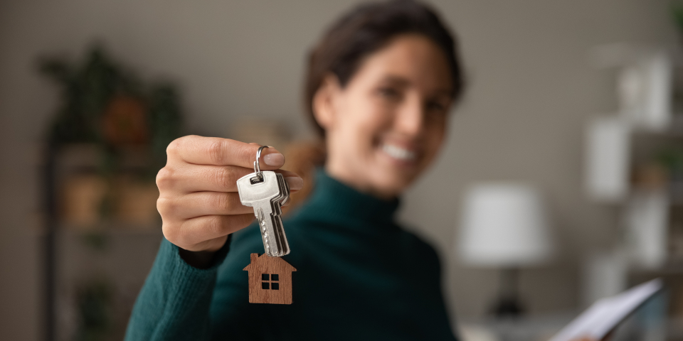 Close up focus on keys, smiling woman realtor selling apartment, offering to client, showing at camera, holding documents, contract, making purchasing deal, real estate agent, mortgage or rent